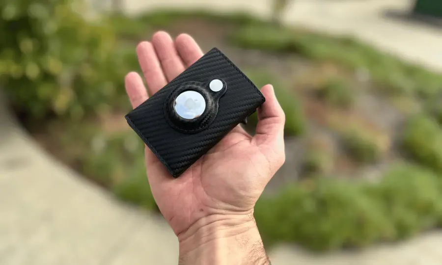 SafeTrack Wallet in carbon fiber with an AirTag slot, held in one hand outdoors